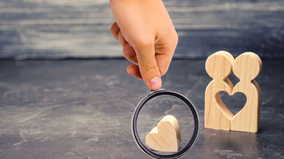 Persona con una lupa y figuritas de una pareja de madera y un corazón